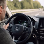 Driver focused on a modern digital dashboard displaying lane assist and adaptive cruise control indicators on a sunny highway.